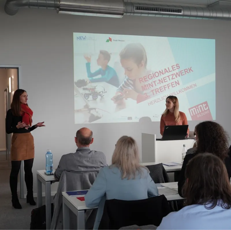 Zwei Frauen präsentieren beim regionalen MINT-Netzwerktreffen vor Publikum mit Projektion.