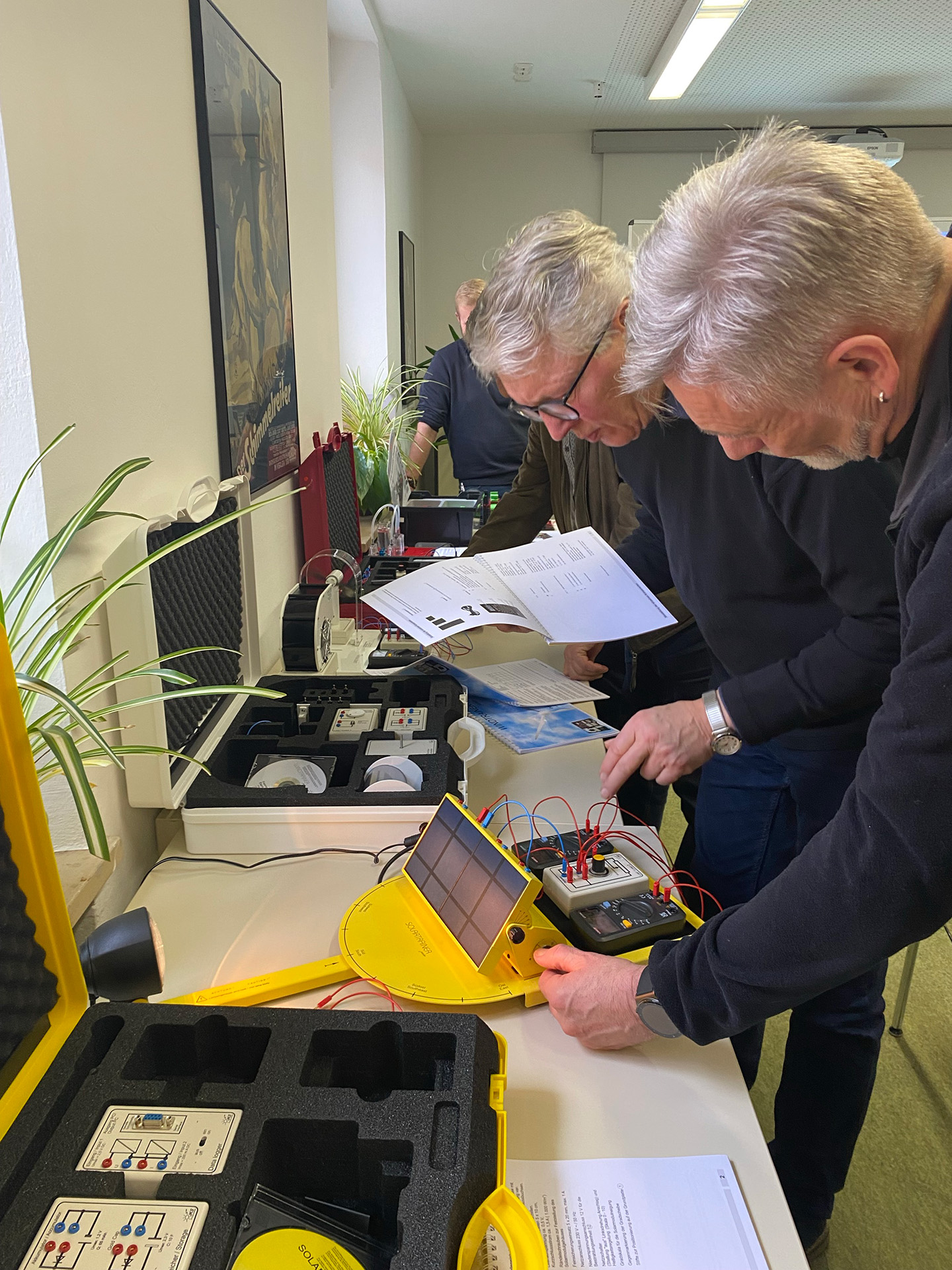 Zwei Männer experimentieren mit einem Solarmodul und prüfen eine Anleitung im Laborraum.