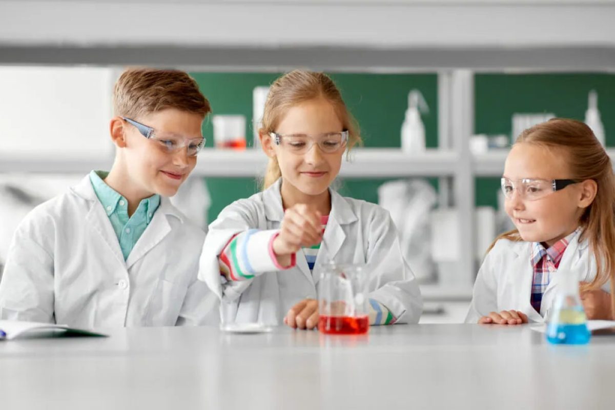 MINT Angebote und Mitmachen Drei Kinder im Laborkittel machen ein Experiment mit farbigen Flüssigkeiten im Chemielabor.