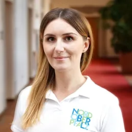 Junge Frau mit langen Haaren trägt Polo mit „Nordoberpfalz“-Logo und steht in einem Flur.