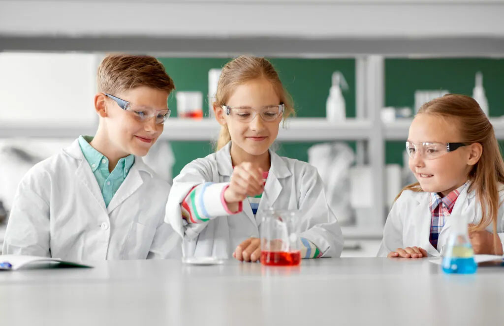 Drei Kinder im Laborkittel machen ein Experiment mit farbigen Flüssigkeiten im Chemielabor.