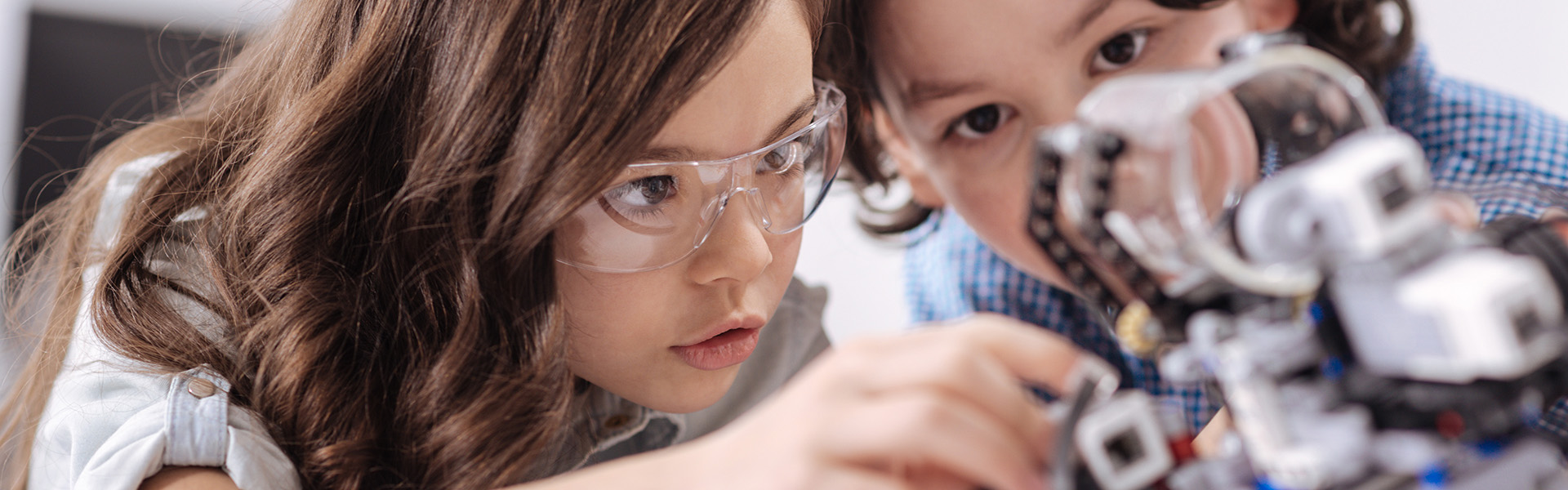 Zwei Kinder bauen konzentriert an einem Roboter. Eines trägt eine Schutzbrille.