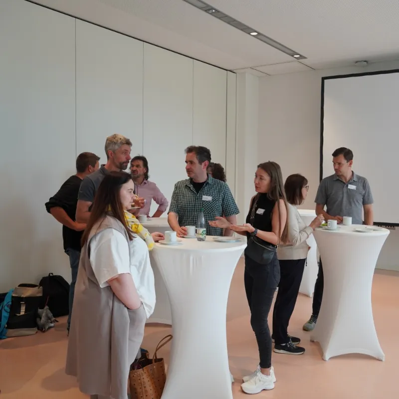 Menschen unterhalten sich bei Kaffee und Stehtischen während einer Netzwerkpause in heller Umgebung.