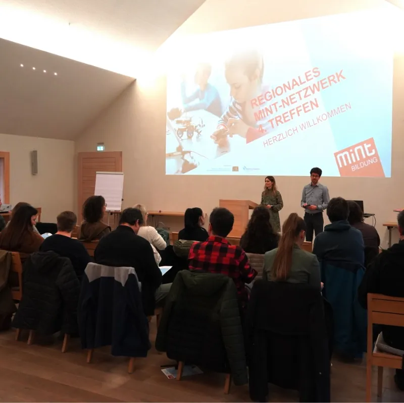 Vortragende begrüßen Teilnehmende beim regionalen MINT-Netzwerktreffen mit großer Präsentation.
