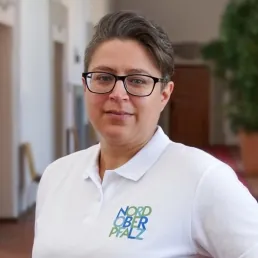 Junge Frau mit Brille und Kurzhaarschnitt trägt Polo mit Logo „Nordoberpfalz“ in einem Flur.