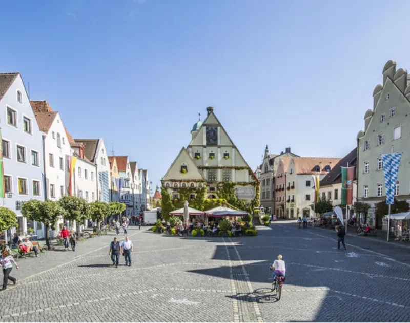 Marktplatz Weiden mit grünem Rathaus, Giebelhäusern, Café, Passanten und bayerischen Fahnen.